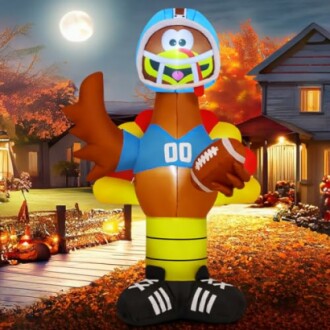 Inflatable turkey dressed as a football player in a yard with autumn decor.